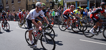 Tour de France competitors ride past the front gates of Downing College